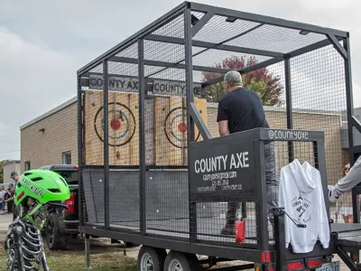 A man throws an axe at a target in a caged trailer.