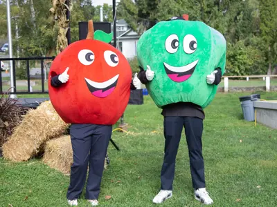A red and green apple mascot with large smiles stand in front of a stage.